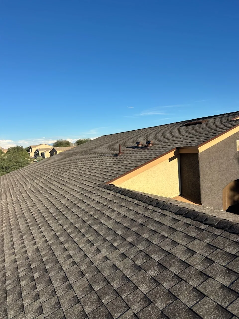 Finished shingle roof around a stucco dormer under a clear sky