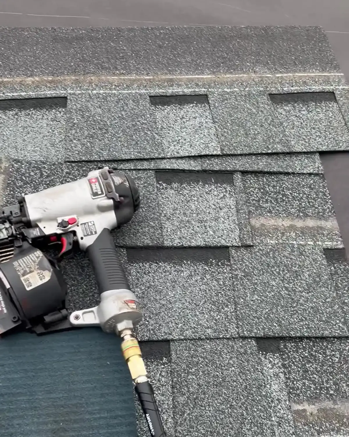 A roofing nailer resting on newly laid grey architectural shingles